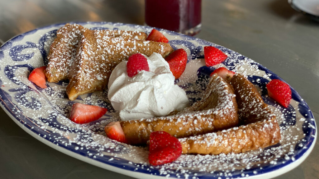 French Toast on a plate with whipped cream, strawberries, and powdered sugar